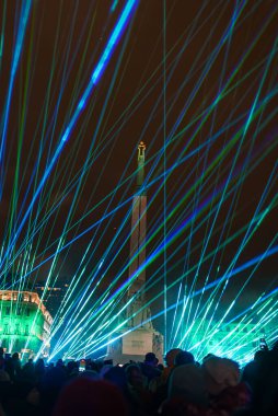 Canlı bir ışık gösterisi, Latvias Bağımsızlık Günü 'nü aydınlatıyor. Mavi ve yeşil lazerler Rigas Özgürlük Anıtı' nın üzerinde gökyüzünü aydınlatıyor. Siluetteki izleyiciler şenlik havasını arttırır..