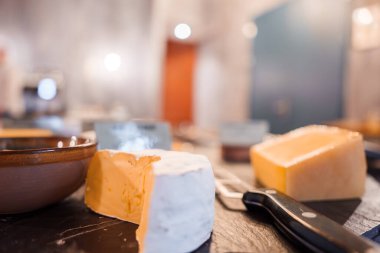 Bir dilim Brie ya da Camembert peyniri, bir dilim Gouda veya Cheddar peyniri, bir peynir bıçağı ve muhtemelen Engelberg 'de sıcak, bulanık bir arka planda bir kase ile yakın plan peynir çeşitliliği..