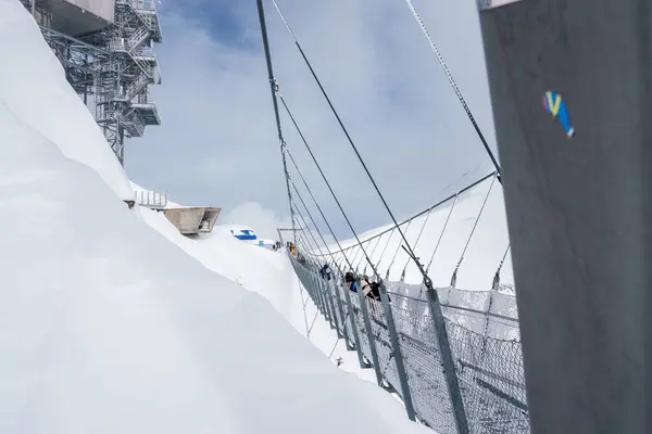 スイスのエンゲルベルクの静かな雪景色で 冬のギヤの訪問者が使用するメッシュフェンシングを備えた金属ケーブルブリッジ バックグラウンドのスキーリゾートインフラストラクチャー — ストック写真
