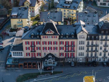 Aerial view of the grand Hotel Bellevue with a red facade in Engelberg, featuring a European alpine design, whitetrimmed windows, and a semicircular canopy entrance. clipart
