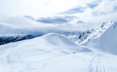 Verbier, Switzerlands 'ın havadan çekilmiş görüntüsü el değmemiş, dalgalı arazide kayak izleri olan karla kaplı bir manzara. Parçalı bulutlu gökyüzü gölgeler bırakır, dağların güzelliğini arttırır..