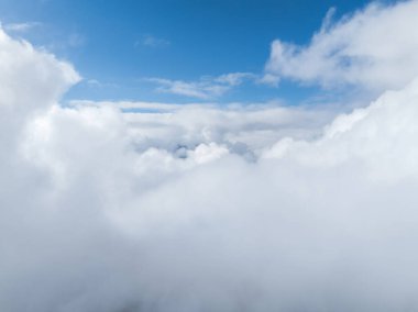 Aerial view of dense, white clouds covering Verbier, Switzerland, with a clear blue sky above, indicating high altitude and fair weather. Details of the town and landscape are obscured. clipart