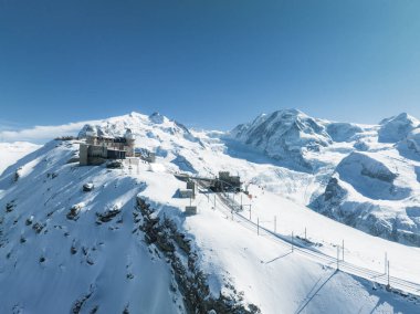 Zermatt 'ın, Switzerlands' ın karlı dağlarının, dar bir pistte bir trenin ve kayak asansörünün çarpıcı bir görüntüsü. Açık mavi gökyüzü ve derin kar kış sporlarını gözler önüne seriyor..