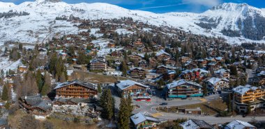 Verbier, İsviçre, yukarıdan bakıldığında, karlı dağlarda bir kayak kasabasını gözler önüne seriyor. Çam, kar ve alp kiraz ağaçlarını karıştırır. Kırmızı otobüsü olan bir yol, hoş geldin kayak merkezi atmosferine ekleniyor..
