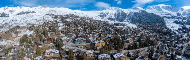Aerial shot of Verbier, Switzerland shows a calm ski town with chalet style buildings among snow peaks. It looks like early winter or spring, perfect for skiing. clipart