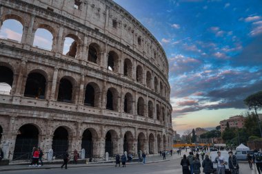 Roma, İtalya 'daki Iconic antik Colosseum, büyük dış kemerleri, kısmen korunmuş duvar. Turistlerle, güvenlik bariyerleriyle, bulutlu gökyüzüyle dolu. Tipik tarihi eser ziyareti..