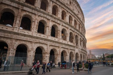 Roma, İtalya 'daki antik kolezyum. Kemerli taş duvarları yaşını ve havasını gösteriyor. Turistler ve yerliler bulutlu bir günde tarihi bir dönüm noktası ile uğraşıyorlar..