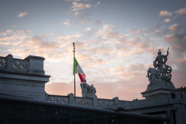 Pembe ve turuncu renklerle boyanmış huzurlu bir gökyüzü ve hafif bir İtalyan bayrağı rüzgarda dalgalanıyor. Süslü heykeller ve mimari ayrıntılar İtalya 'da önemli tarihi bir yere işaret ediyor.