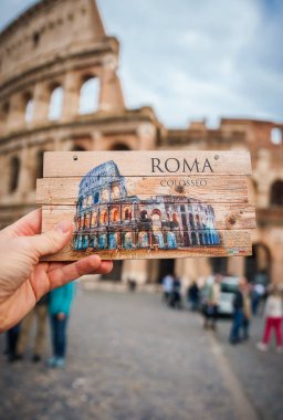 Roma, İtalya 'da gerçek Colosseum' a karşı ROMA ve COLOSSEO ile el ele tutuşan ahşap hatıra. İnsanlarla sanatsal görsel efekt ve bulutlu gökyüzü.