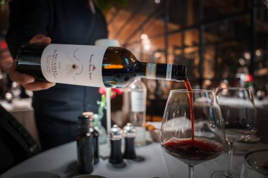 Samimi lüks restoran dekorasyonu, şarap kadehine dökülen kırmızı şarap, şişe ve cama odaklanma, lüks yemek, takım elbise servisi, samimi ortam, zarif masa ayarları..