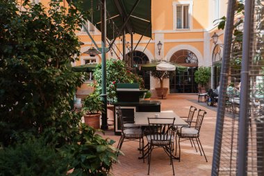 Roma 'da bir otelde yemyeşil bitkiler ve şemsiyeli masalarla lüks bir açık hava oturma alanı. Klasik İtalyan mimarisi ve rahat ışıklandırma sakin bir geri çekilme yaratıyor.