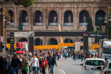 Tarihsel bir caddede çeşitli kalabalıkların yürüdüğü, klasik ve modern unsurları harmanlayan araçlar ve ticari tabelalarla dolu bir Avrupa şehrindeki şehir manzarası..