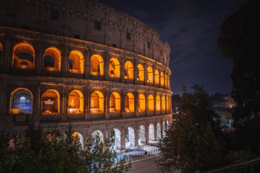 Kolezyum, İtalya, Roma 'daki Flavian Amfitiyatrosu, gece çekilmiş. Ilık ışıkla aydınlatılmış, büyük mimarisi ve karmaşık ayrıntıları vurgulanmış. Sakin, görkemli bir atmosfer..