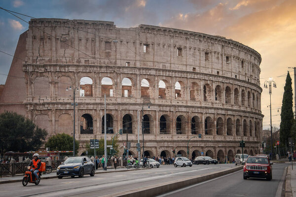 Iconic view of the ancient Colosseum in Rome, Italy. Cloudy day with arches and levels visible. Modern street scene in foreground adds vibrant contrast.