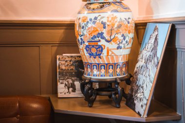 Dekoratif seramik vazo mavi, turuncu desenli ahşap tezgah, Kronleuchte vor der Jungfrau 'lu Almanca kitap, Alpler temalı eşya, rahat iç dekorasyonlu deri koltuk köşesi, konumu yok..