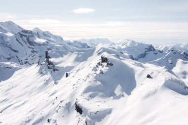 İsviçre 'nin Murren kayak merkezindeki kar kaplı zirvelerin nefes kesici manzarası. Temiz gökyüzünün altında el değmemiş beyaz kar örtüleri engebeli arazi, görünürde kayakçı yok. Büyük dağ sırası ufka doğru uzanıyor..