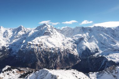 İsviçre Alpleri 'ndeki kar kaplı tepelerin nefes kesici manzarası, muhtemelen Murren kayak merkezinden alındı. Görkemli dağlar yeryüzüne hakim, güneş ışığıyla yıkanmış..