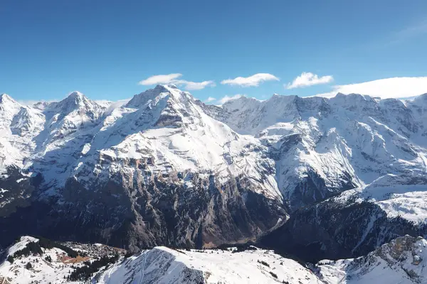 İsviçre Alpleri 'ndeki kar kaplı tepelerin nefes kesici manzarası, muhtemelen Murren kayak merkezinden alındı. Görkemli dağlar yeryüzüne hakim, güneş ışığıyla yıkanmış..