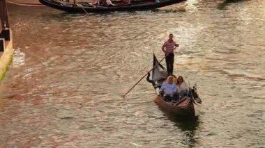 Venedikli gondolcu Venedik İtalya 'nın yeşil kanal sularında gondola biniyor. Ünlü Canal Grande 'deki geleneksel Gondol manzarası gün batımında romantik altın bir akşam ışığı altında.
