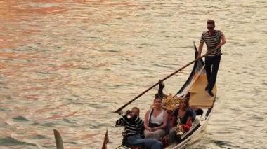 Venedikli gondolcu Venedik İtalya 'nın yeşil kanal sularında gondola biniyor. Ünlü Canal Grande 'deki geleneksel Gondol manzarası gün batımında romantik altın bir akşam ışığı altında.