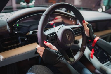 Modern tasarım ve çok fonksiyonlu Porsche direksiyon simidine yakından bakın. Sürücü elleri ve kırmızı çiviler. Kırmızı emniyet kemeri, parlak gösterge paneli.