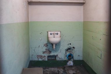 Alcatraz hapishanesinde terk edilmiş bir oda. Beyaz ve soluk yeşille boyanmış, su tesisatı, hasarlı duvarlar, yıpranmış döşemeler. Tarihsel ihmali çağrıştırıyor.