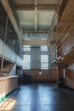 San Francisco, ABD 'deki Alcatraz hapishanesinin iç manzarası. Geniş tavanlı, büyük pencereli, yaşlanmış şeftali duvarlı, iki katmanlı hücre bloklu, açık hücreli, yürüyüş yolu, tezgahın arkasında rehber..