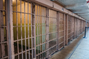 San Francisco, ABD 'de 402 gibi numaralarla işaretlenmiş hücrelerde paslanmış bej çubukları olan Alcatraz hapishane koridoru. Boyanın soyulmasında tarihsel bozulma görülür..