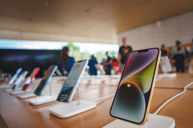 Mountain View, CA 'da bir Apple mağazasının içinde. iPhone 'lar düzgünce bir masaya yerleştirilmiş, bazı müşteriler ve personel görülebilir. Apple ürünlerini sergileyen modern, yoğun perakende ortamı.