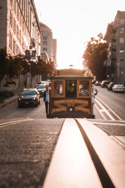Gün batımında Powell ve Hyde Caddelerindeki Iconic San Francisco teleferiği yolcuları yolculuğun tadını çıkarıyor. Klasik mimari, altın ışık, otantik şehir manzarası..