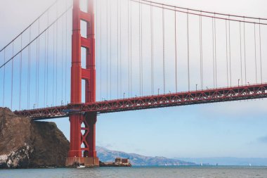 San Francisco, Kaliforniya 'daki Iconic Golden Gate Köprüsü. Aşağıdan bakıldığında kırmızı turuncu yapı, simetrik kablolar, kayalık çıkıntılar ve uzak topraklar görünüyor..