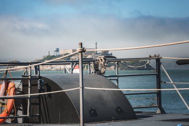 Close up view of a boat deck with maritime equipment, focused on a black structure. Golden Gate Bridge and Alcatraz Island in blurred background. Captures essence of San Francisco Bay area. clipart