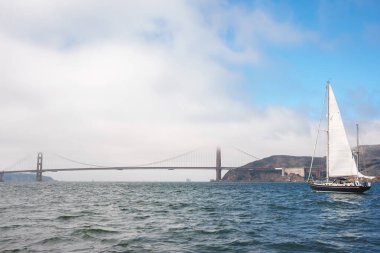 Golden Gate Köprüsü 'nün altında sisli beyaz yelkenli ile San Francisco Körfezi' nin sakin manzarası. Yansıtıcı su ve arka planda yuvarlanan tepeler. Tipik turistik yer..