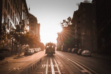Scenic San Francisco street during sunset. Golden light, long shadows, iconic cable car, parked cars, bay windows, ornate facades. Serene urban landscape. clipart