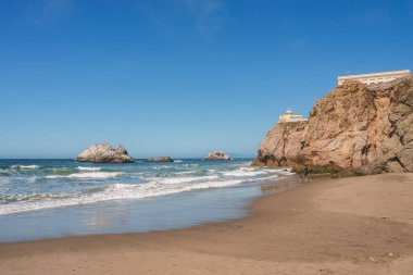 Sakin San Francisco sahnesi, kumlu sahil, dalgalar, kayalar ve tepesinde bir bina olan bir uçurum. Çok az kişiyle huzurlu bir ortam..