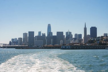 San Francisco 'nun gündüz manzarası, Transamerica Piramidi ve Satış Gücü Kulesi gibi ikonik binaları gösteriyor. Berrak mavi gökyüzünün altında sakin bir rıhtım manzarası.