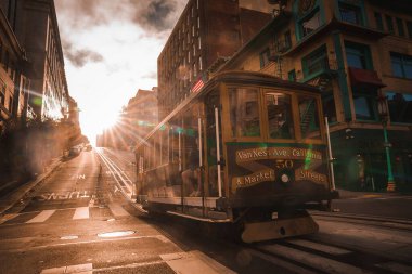 Classic cable car in San Francisco, Van Ness Ave California St. sign visible, moving on steep street. Sun creates dramatic lighting, iconic city charm captured. clipart