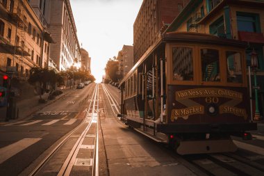 Iconic San Francisco cable car on steep incline at Van Ness Ave. and Market St. Golden sunlight casts long shadows on historic city street, no tourists. clipart