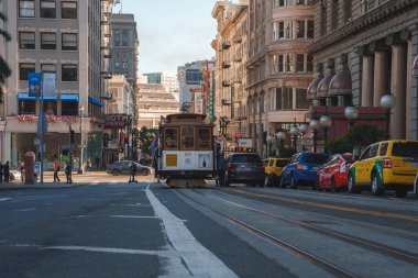 Iconic cream and maroon cable car in bustling San Francisco. Mix of modern and classic architecture, busy street with vehicles and pedestrians, late afternoon atmosphere. Rich history and growth. clipart