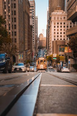 Iconic cable car travels along steep San Francisco street lined with buildings. Classic hue, bustling cityscape, busy street life, urban canyon backdrop. clipart
