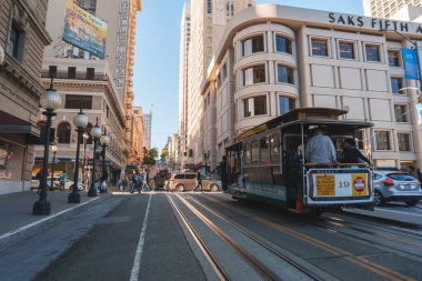 Classic San Francisco scene with iconic cable car in foreground on city street. Mix of modern, older buildings, hilly terrain, blue sky, and lively vibe. clipart
