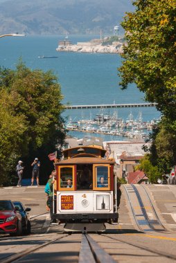 Iconic San Francisco teleferiği dik bir tepeye tırmanıyor. Tahta araba 4, deniz kenarı, marina, Alcatraz Adası manzaralı manzaralı manzaralı bir yolculuk sunuyor. Güneşli bir gün, bekleyen turistler.