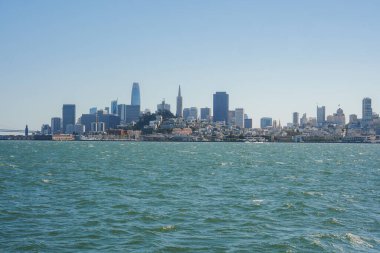 Körfez boyunca uzanan San Francisco siluetinin panoramik görüntüsü açık mavi gökyüzüne karşı bir siluet oluşturuyor. Görünürde sis, ikonik köprü ya da tekne yok..