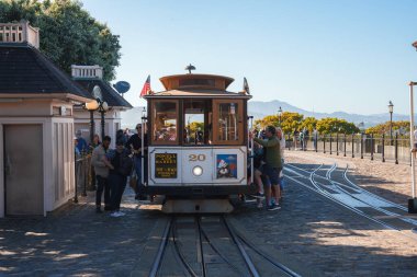 Iconic cable car in San Francisco, passengers boarding, city atmosphere with tourists, clear skies, urban setting with historic charm near popular spot. clipart