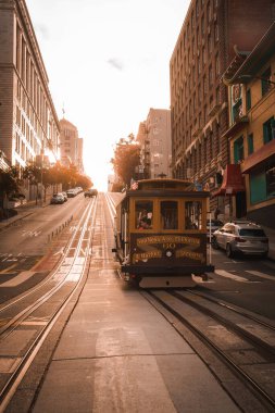 Iconic San Francisco cable car on steel tracks with warm sunlight, reflecting citys architecture. Powell Hyde line, tourists on board, serene street scene. clipart