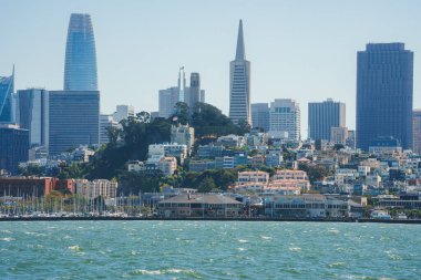 San Franciscos 'un parlak körfez suları, yatları, tarihi rıhtım binaları ve ikonik gökdelenlerin yer aldığı modern şehir silueti manzarası..