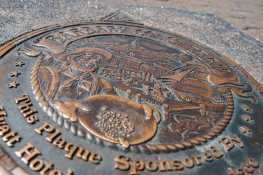 Close up view of circular plaque on ground with historical figure holding navigational instrument, Barbary Coast Trail text. Likely in San Francisco, CA. clipart