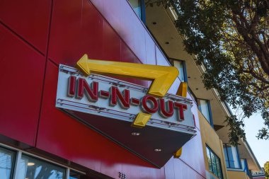 San Francisco 'daki Iconic In N Out Burger tabelasında. Kırmızı duvarda sarı ok logosu, beyaz harflerle marka adı, düşük açılı çekim, renkli bina ipuçları..