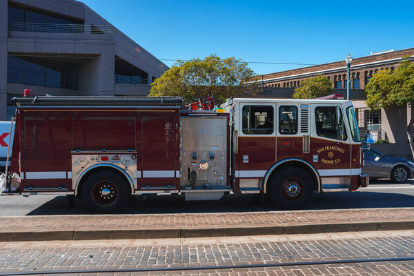 Пожарная машина Сан-Франциско припаркована на городской улице, красный автомобиль с пожарным департаментом Сан-Франциско. на стороне. Современное здание и голубое небо на заднем плане.