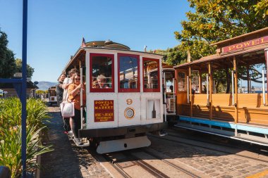 Classic San Francisco cable car, number 9 on Powell Hyde line. Iconic red and white design, passengers holding poles. Tourist hotspot with lush greenery and sunny skies. clipart